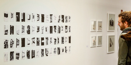 Ein Mann betrachtet kleine Drucke an der Wand in einer Ausstellung.